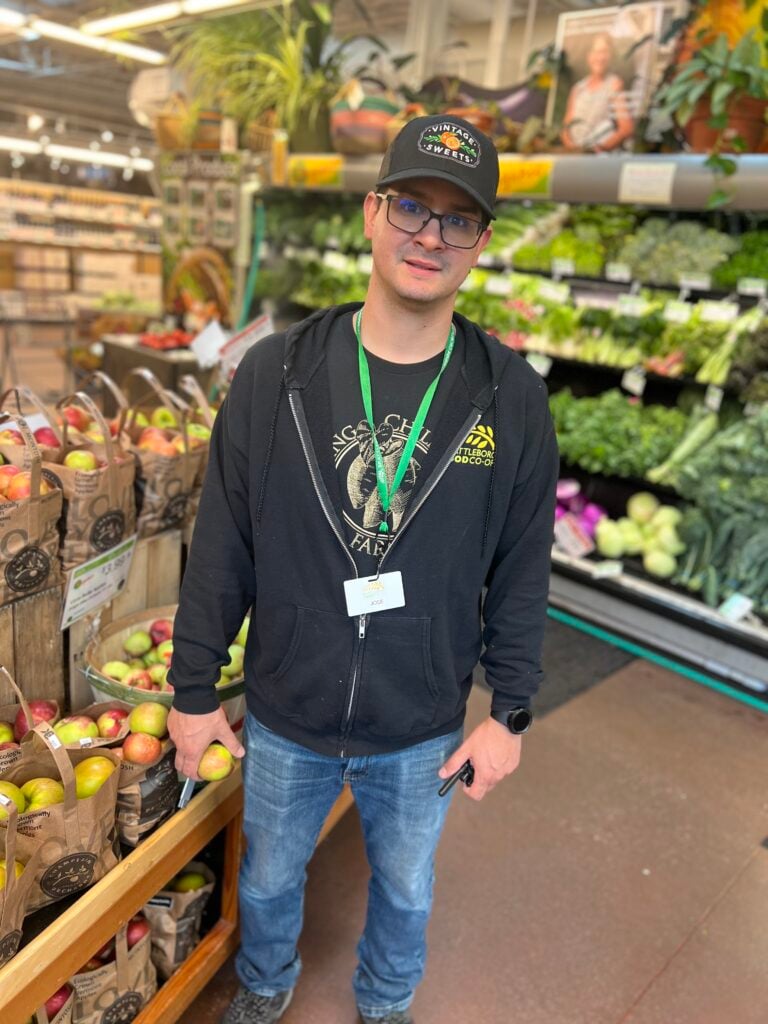 A photo of Jose, the assistant manager of the BFC Produce department, standing in front of the apple totes